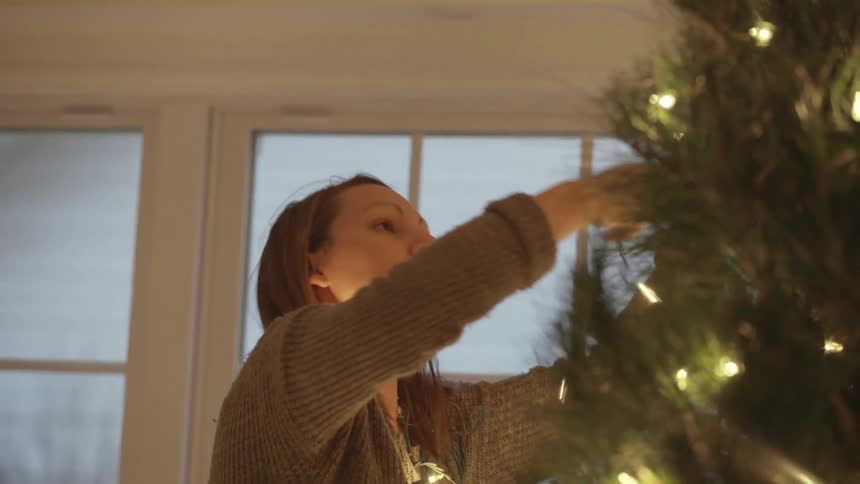 A woman hangs lights on a christmas tree