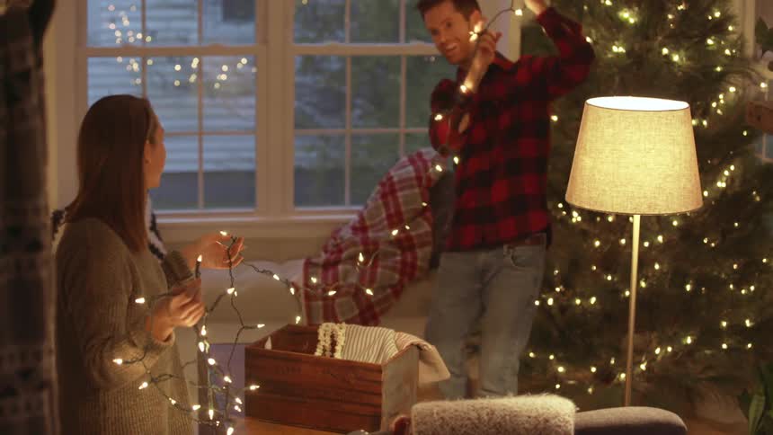 A couple are smiling and laughing as they hang christmas lights