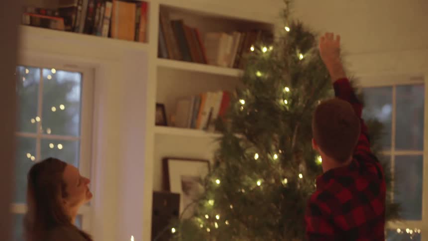 A man and woman hang lights on a christmas tree