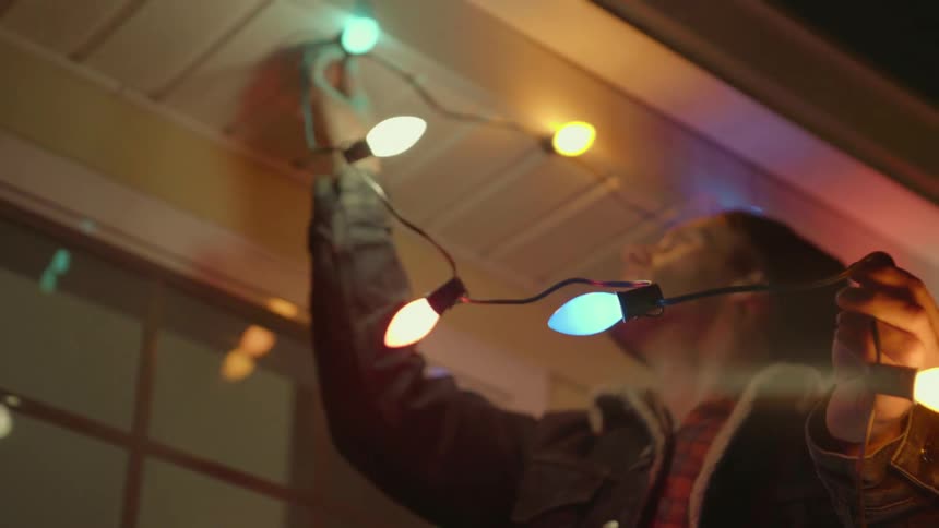 A man is hanging christmas lights on the house roof