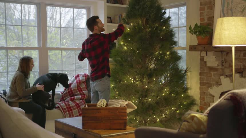 A man and woman decorate a christmas tree