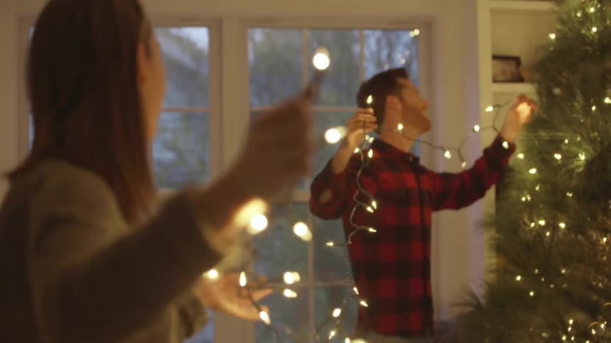 A man and woman are holding christmas lights and applying them to the tree
