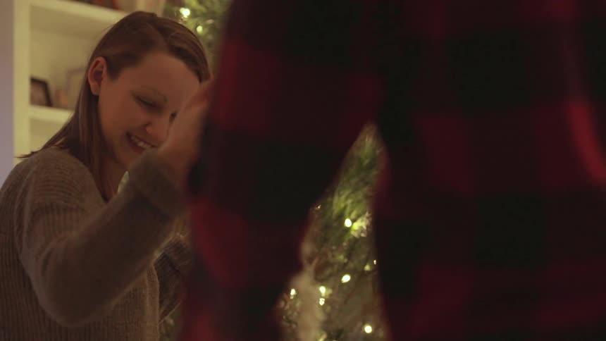 A man and woman hang popcorn garland on a christmas tree