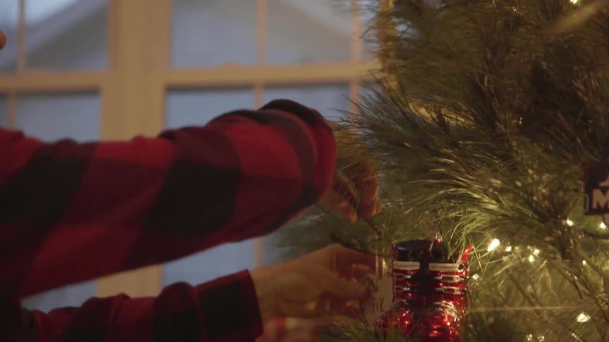 Man hanging an ornament on his christmas tree to decorate