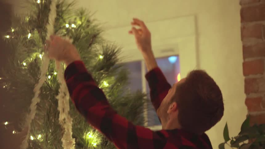 A woman holds a popcorn string as a man decorates the tree with it
