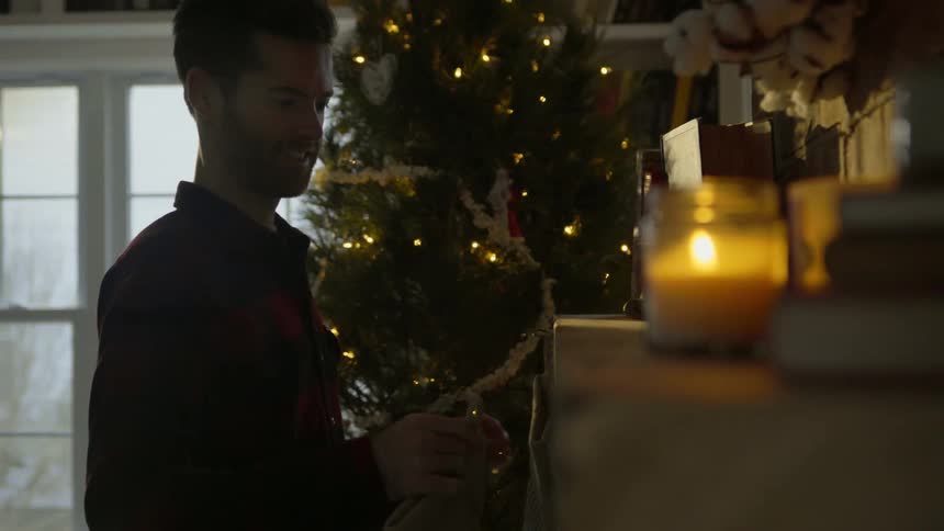 A man hangs stockings on the mantel near the tree