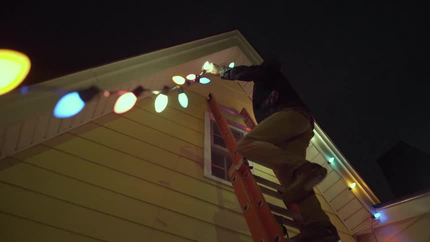 A man hangs christmas lights on a house