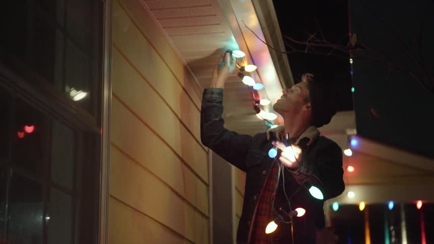 A man hangs christmas lights on a house