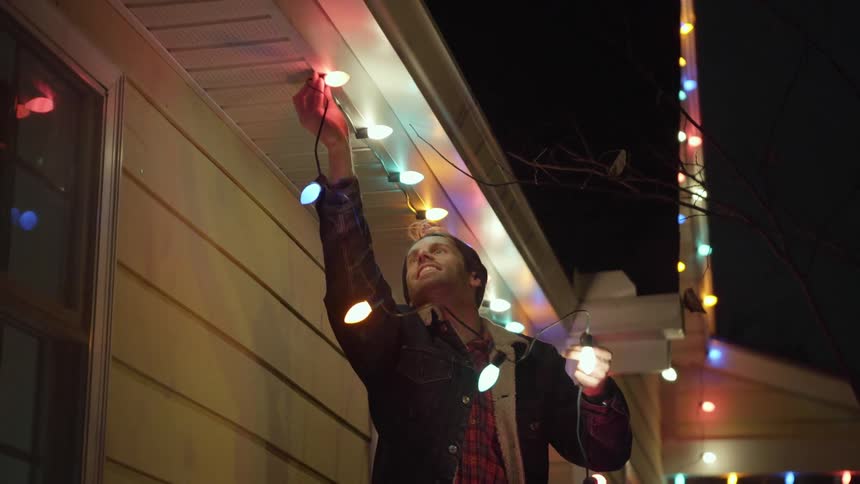 A man is hanging christmas lights outside at night