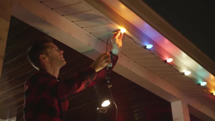 A man is hanging multi colored lights from the roof