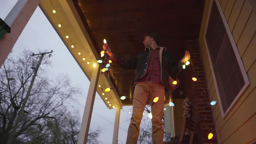 A man hangs christmas lights on a house
