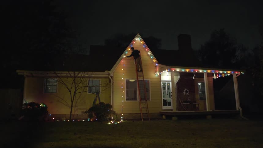 A man hangs christmas lights on a house