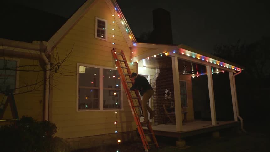 A man hangs christmas lights on a house