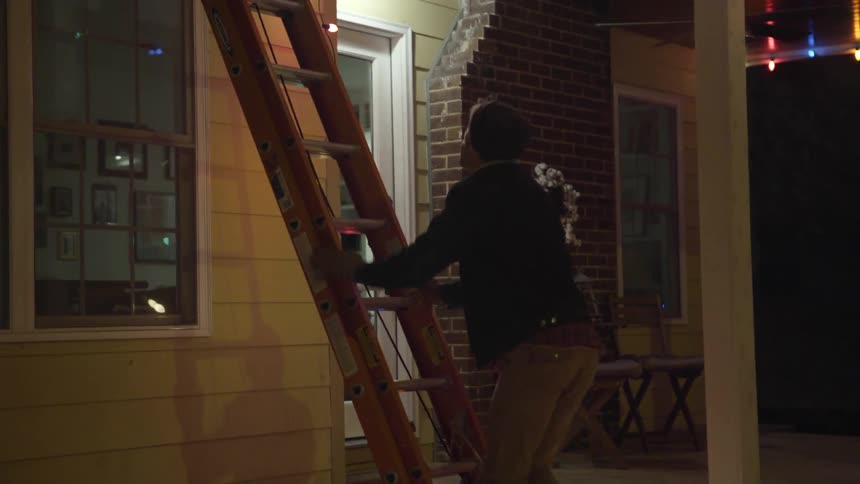 A man leans a ladder against the house and climbs up