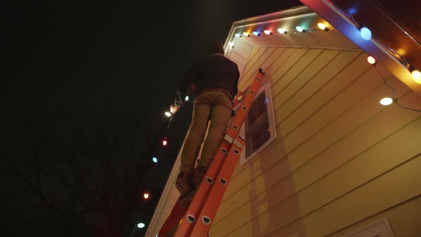 A man is on a ladder hanging christmas lights