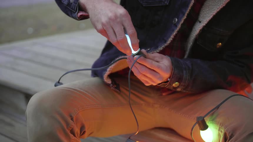 A man screws a lightbulb into a strand of Christmas lights