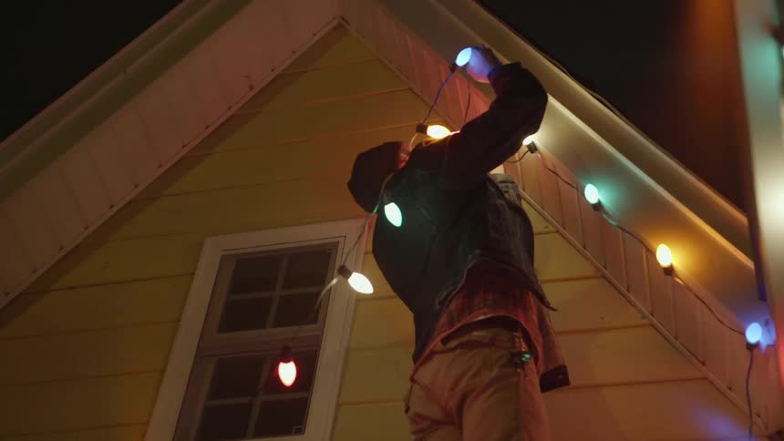 Man hanging christmas lights on his house at night