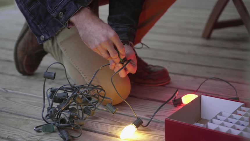 A man is replacing the bulbs on his string of christmas lights at dusk