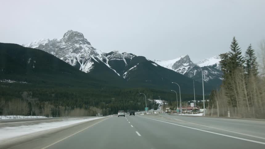 Cars are travelling on the road leading towards the snow covered mountains