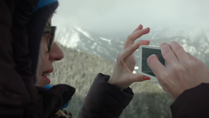 A person wearing glasses takes pictures of a snow covered mountain with their phone