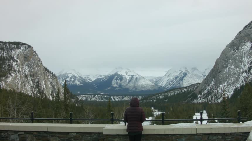 A person stands in the balcony and enjoys the picturesque landscape of snow covered mountains