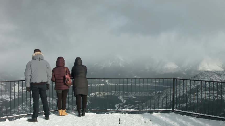 Three persons stand at the balcony and enjoy the view of the snow covered mountains