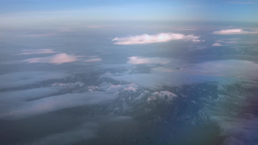 Snow covered mountains are seen through clouds in an aerial view