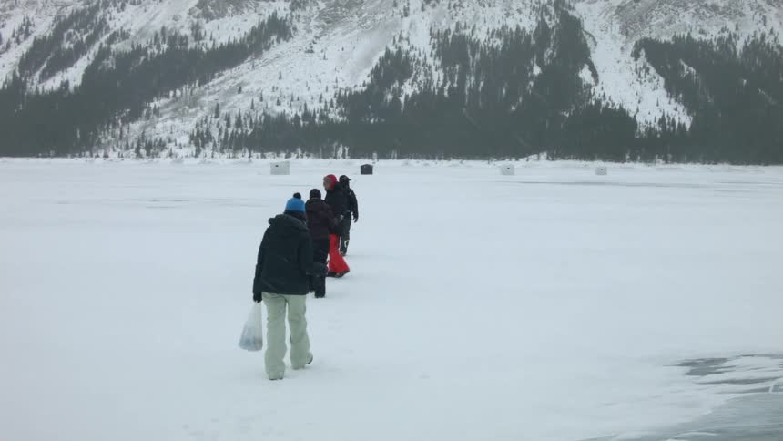 People walk across a snow covered field towards a mountain