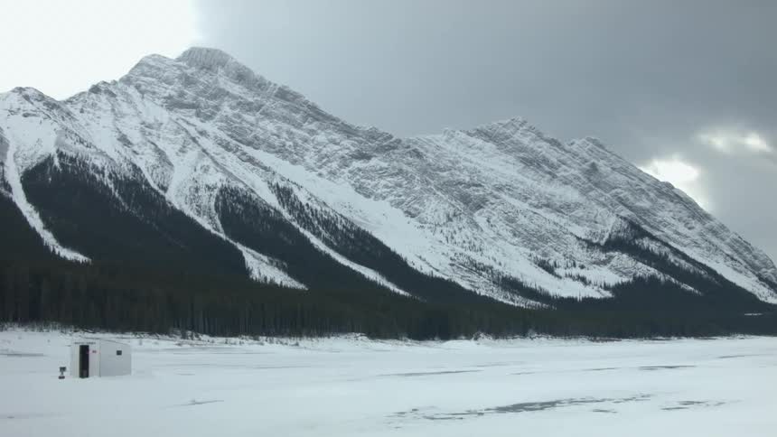An ice fishing shack is shown below a mountain