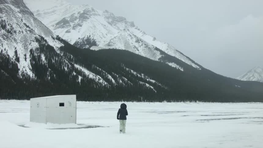 A woman walks across a field of snow towards snow-covered mountains