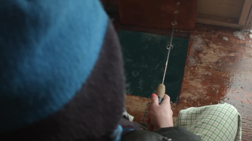 A person spins the reel of a fishing pole while they ice fish