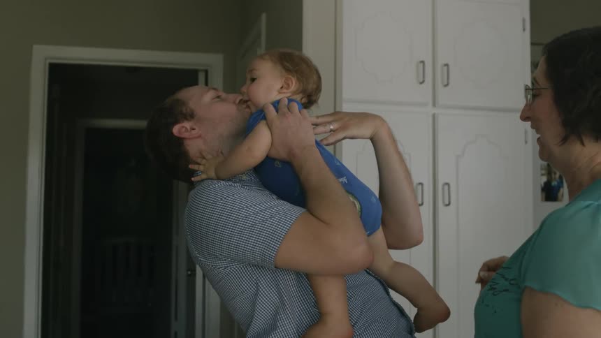 A woman hands a baby to a man who hugs and kisses him