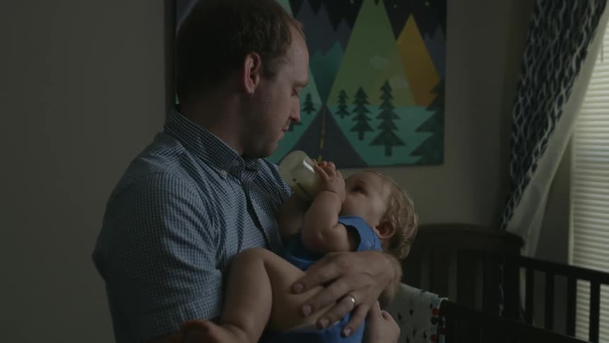 A baby drinks a bottle while being rocked in his dad's arms