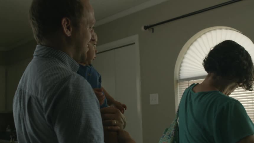 A man holding a baby waves goodbye to a woman