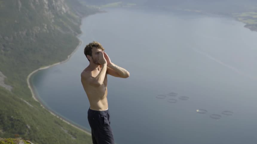 Active male hiker stretching after reaching a high mountain summit on a cloudy day.