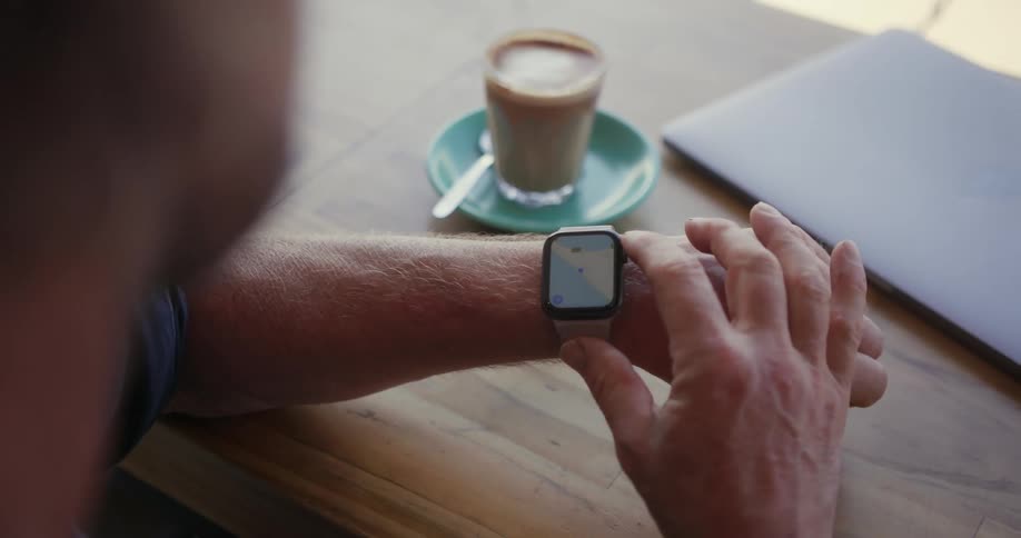 A man looks down and uses his smartwatch in a cafe
