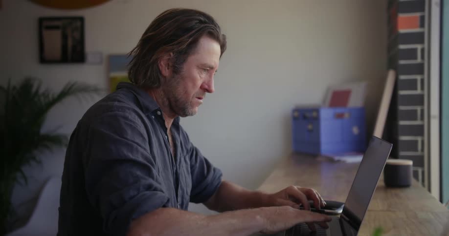 A man uses a laptop on a table by the window