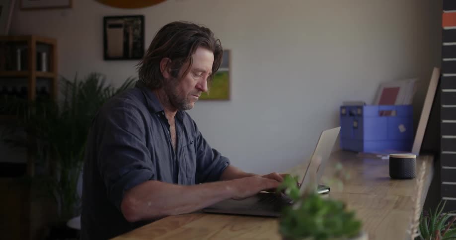 A man is sitting at a counter working on a laptop during the day
