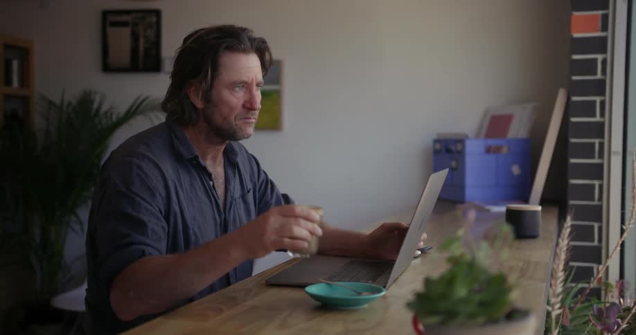 A man sips on a drink while working on a laptop