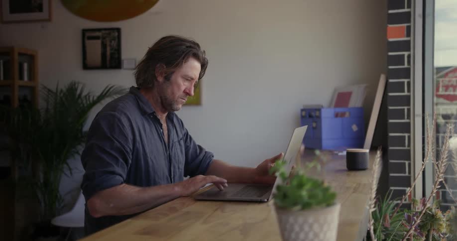 A man sitting at a counter is working on a laptop during the day