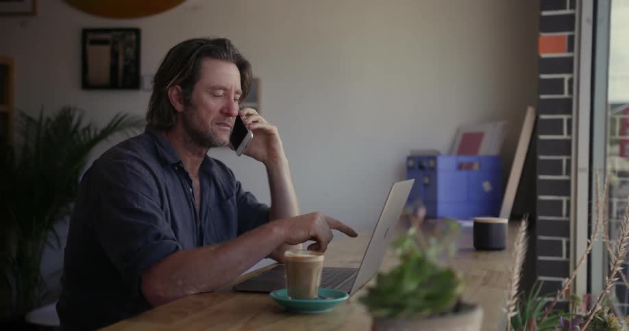 A man talks on a phone while working on a laptop