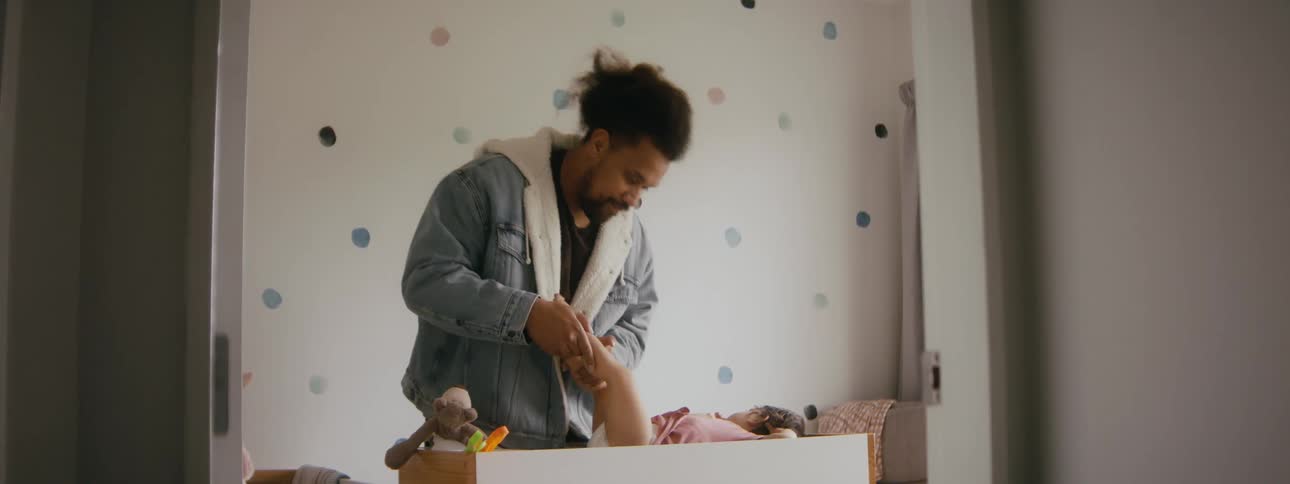 Father getting ready to change the diaper of his young daughter who is lying down in the cradle in the middle of the room