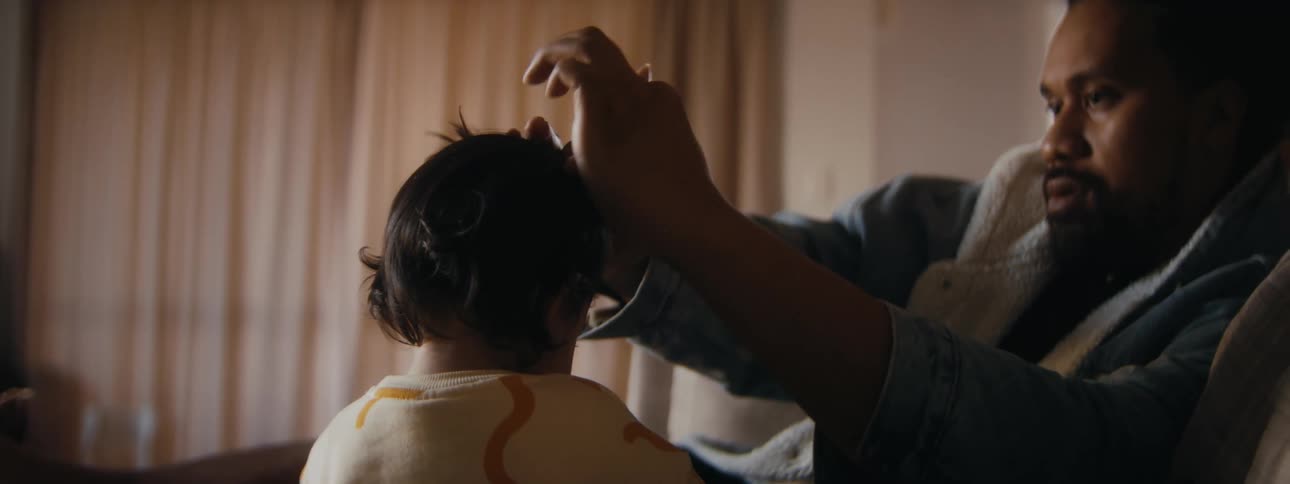 A man ties the hair of a young girl before she crawls out of his lap