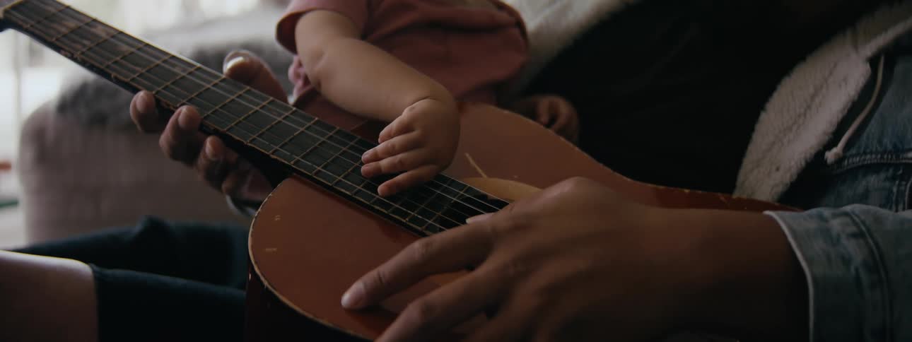 A father holding a baby and strumming a guitar
