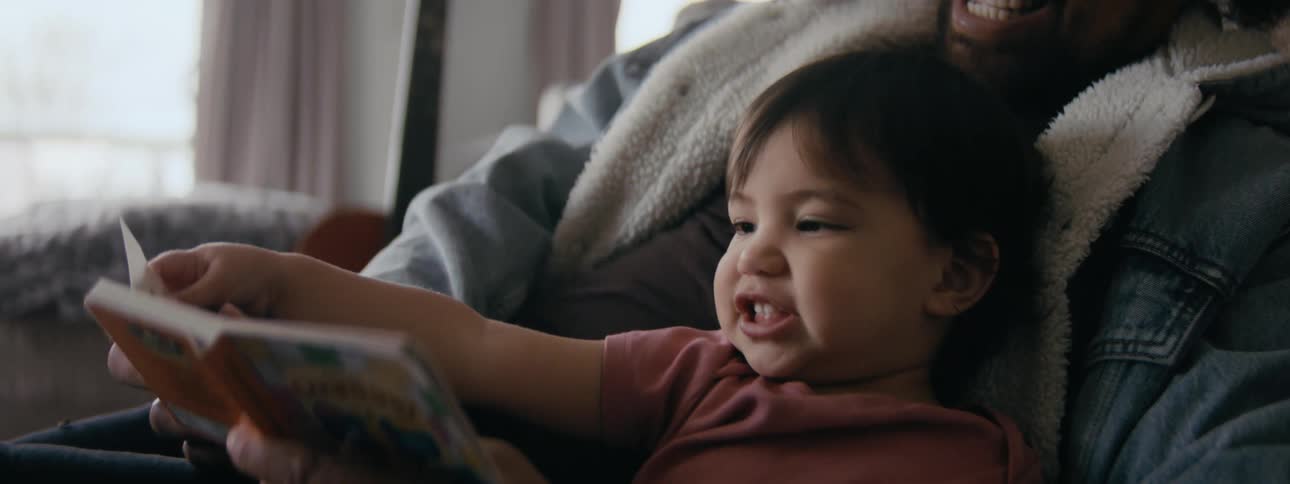 Baby makes faces and points as dad reads her a story