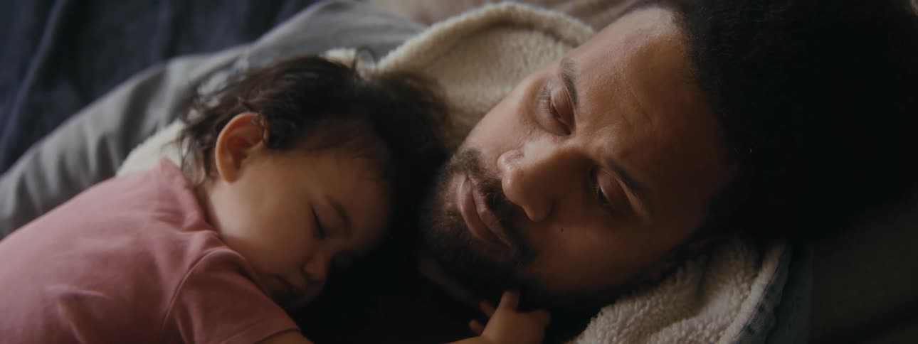 Thoughtful father lying down with his small daughter sleeping on his chest