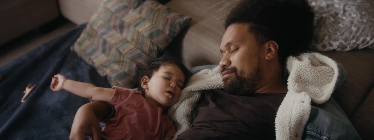 A toddler is taking a nap with her dad on the couch