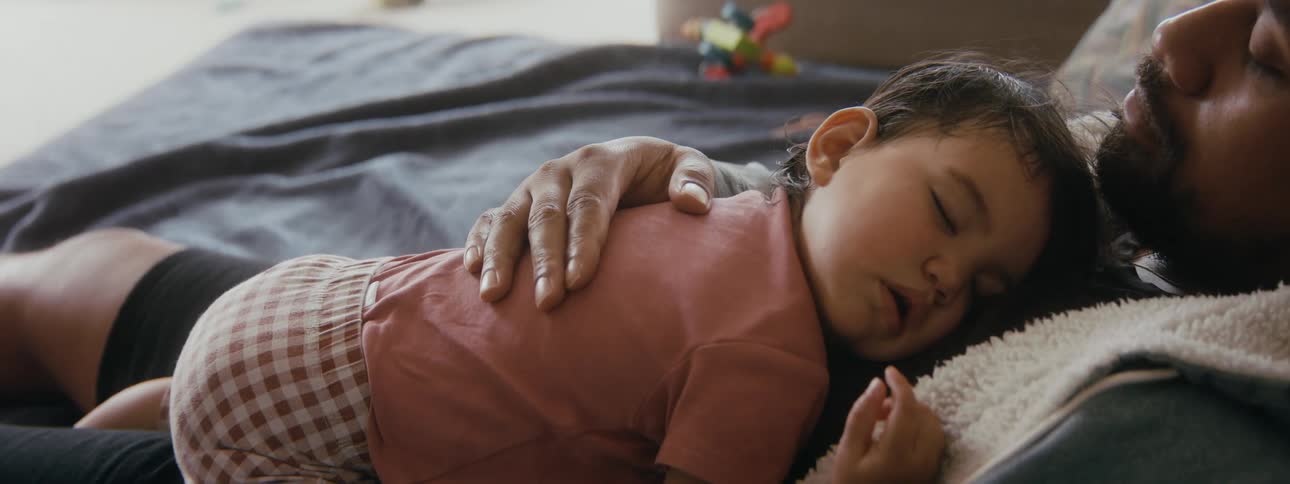 A newborn is napping on her father indoors