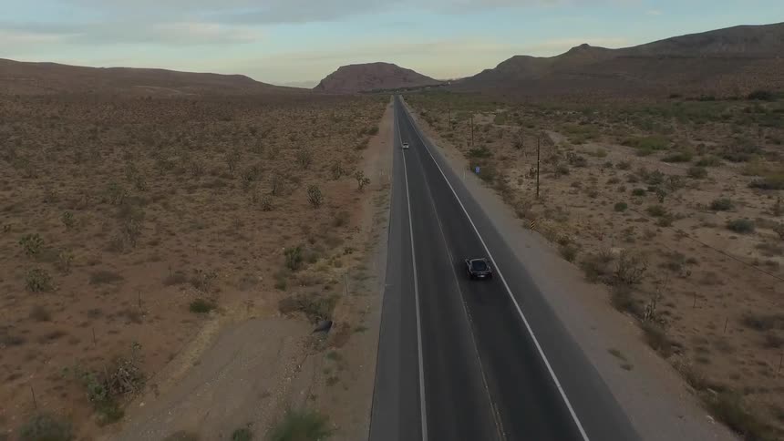 A black vehicle is moving down a road near a desert