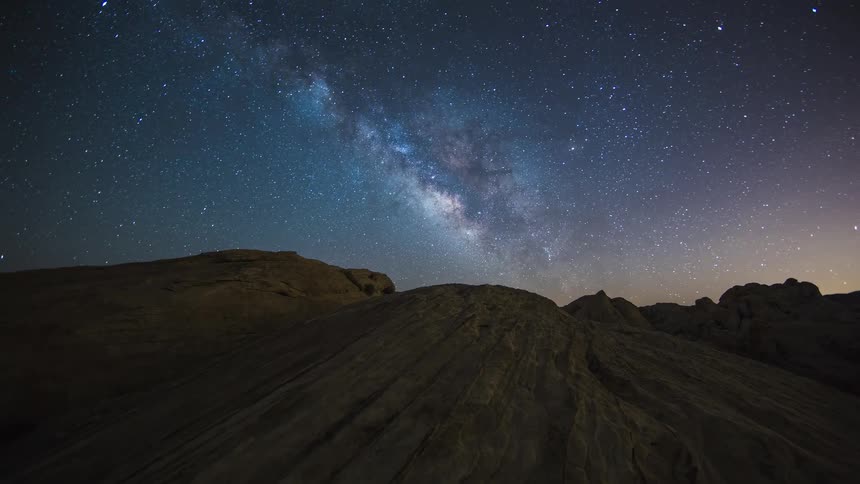 Stars of the milky way shine brightly as they move over mountains across the night sky